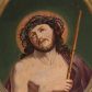Zdjęcie nr 1: Owalny obraz z przedstawieniem Chrystusa w typie Ecce Homo. Jezus ukazany w półfigurze, zwrócony w trzech czwartych w lewo. Prawą ręką przytrzymuje trzcinę, lewą ma schowaną pod płaszczem. Wznosi wzrok ku górze, ma owalną, okoloną zarostem twarz, ciemne oczy, wąski nos oraz rozchylone usta. Długie, jasnobrązowe włosy spływają mu na plecy i lewe ramię. Na głowie korona cierniowa, wokół której rozświetlony na czerwono nimb. Purpurowy, przerzucony przez lewe ramię płaszcz spływa gęstymi fałdami w dół. Tło ciemnozielone.