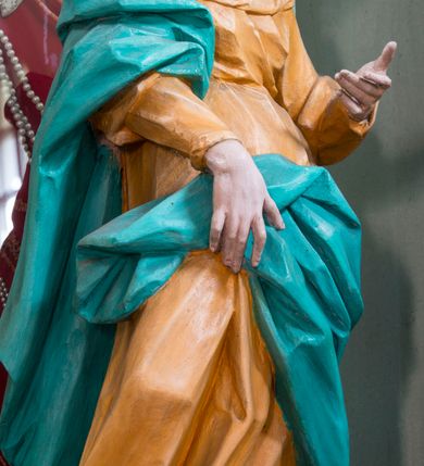 Zdjęcie nr 2: Rzeźba pełna, ustawiona na niewielkim cokole. Figura ukazana w całej postaci, zwrócona w trzech czwartych w lewo, w silnym kontrapoście, o esowato wygiętej sylwetce. Głowa delikatnie pochylona, skierowana w lewo; lewa ręka ugięta i uniesiona, prawa opuszczona z przodu, podtrzymuje płaszcz. Twarz szczupła, o wyraźnie zaznaczonej linii brody i kości policzkowych, oczy duże, płytko rzeźbione, nos niewielki. Święta jest ubrana w sięgającą ziemi,  żółtą suknię, przepasaną w talii, z wąskimi rękawami oraz dużym dekoltem z wywiniętą partią draperii przy brzegu. Tkanina przylega do ciała, jest marszczona w partii torsu i drapowana dołem w grube, pojedyncze fałdy. Turkusowy płaszcz przerzucony przez prawe przedramię opada przez plecy na lewy bok, z podtrzymywaną z przodu partią tkaniny, draperia silnie fałdowana. Na głowie długi, biały welon opadający na plecy. Polichromia naturalistyczna.
