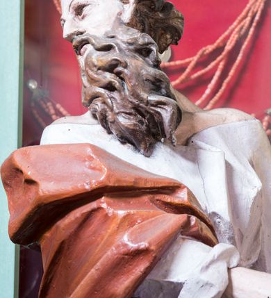 Zdjęcie nr 5: Rzeźba pełna, posadowiona na niskim cokole. Święty ukazany całopostaciowo, zwrócony w prawo, w silnym kontrapoście z prawą nogą odsuniętą do tyłu, z głową ukazaną z profilu, skierowaną w prawo. Obie ręce zwrócone w lewą stronę. Twarz szczupła, pociągła, o wydatnym, wąskim nosie i płytkich oczodołach, okolona długą gęstą brodą i krótkimi układającymi się w pukle włosami jakby rozwianymi do tyłu. Postać jest ubrana w jasną suknię sięgającą stóp, o dużym dekolcie odsłaniającym ramiona. Tkanina przylega do ciała, drapowana jest w grube, pojedyncze fałdy. Okrywający plecy brązowy płaszcz przerzucony przez prawe ramię i lewe biodro jest spięty taśmą na przodzie. Polichromia naturalistyczna.