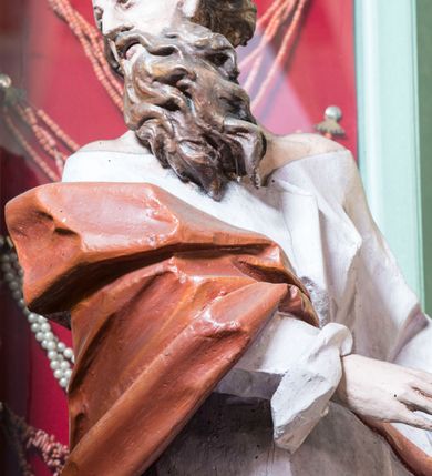Zdjęcie nr 4: Rzeźba pełna, posadowiona na niskim cokole. Święty ukazany całopostaciowo, zwrócony w prawo, w silnym kontrapoście z prawą nogą odsuniętą do tyłu, z głową ukazaną z profilu, skierowaną w prawo. Obie ręce zwrócone w lewą stronę. Twarz szczupła, pociągła, o wydatnym, wąskim nosie i płytkich oczodołach, okolona długą gęstą brodą i krótkimi układającymi się w pukle włosami jakby rozwianymi do tyłu. Postać jest ubrana w jasną suknię sięgającą stóp, o dużym dekolcie odsłaniającym ramiona. Tkanina przylega do ciała, drapowana jest w grube, pojedyncze fałdy. Okrywający plecy brązowy płaszcz przerzucony przez prawe ramię i lewe biodro jest spięty taśmą na przodzie. Polichromia naturalistyczna.