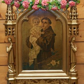 Zdjęcie nr 1: Feretron dwustronny z obrazami Matki Boskiej Częstochowskiej oraz św. Antoniego Padewskiego. Konstrukcja feretronu osadzona na dwóch nóżkach na planie koła, wspierających dwa wieloboczne w rzucie cokoły, połączone listwami stabilizującymi konstrukcję feretronu; cokoły zaopatrzone są w otwory na drążki do noszenia. Na cokołach ustawione dwie rzeźby niezidentyfikowanych świętych lub aniołów, ujętych z profilu, nad nimi nadwieszone baldachimy zwieńczone stylizowanymi kwiatonami. W centrum tej konstrukcji obrazy ujęte w profilowaną ramę, zamkniętą łukiem oślim, zwieńczoną kwiatonem. Na zwieńczeniu feretron zdobiony jest ażurową dekoracją roślinną. Struktura feretronu jest złocona. Po jednej stronie ukazany jest wizerunek Matki Boskiej Częstochowskiej w tradycyjnym typie ikonograficznym. Matka Boska ubrana jest w czerwoną suknię i zielony płaszcz, a Dzieciątko w czerwoną suknię. Szaty są bogato malowane w wici utworzone z koralików i kolorowych kamyków. Pozostałe elementy podobne jak w oryginalnym wizerunku. Tło złote, wokół głowy Matki Boskiej dwanaście gwiazd. Po drugiej stronie feretronu znajduje się obraz św. Antoniego Padewskiego. Święty Antoni ukazany do wysokości trzech czwartych, zwrócony w swoją prawą stronę z Dzieciątkiem Jezus na prawym ręku. Twarz owalna z długim nosem, dużymi oczami o migdałowym kształcie i zarumienionymi policzkami. Ubrany jest w brązowy habit franciszkański, przewiązany sznurem, z różańcem u boku i z tonsurą na głowie. Dzieciątko Jezus zwrócone jest trzy czwarte w lewo, rączkami obejmujące św. Antoniego, z główką skierowaną na wprost. Twarz o rysach dziecięcych, okolona jasnymi i krótkimi włosami. Ubrane jest w białą, długą pieluszkę, spływającą  obficie w dół. Wokół głów postaci rozświetlone na złoto otok. Tło szare. W prawym dolnym narożu obrazu, na obłoku leży gałązka białej lilii.