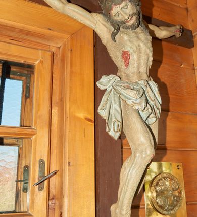 Zdjęcie nr 2: Pełnoplastyczna figura Chrystusa przybita do krzyża trzema gwoździami. Sylwetka postaci esowato wygięta, ukazana w lekkim zwisie, dłonie z zagiętymi palcami małym i serdecznym. Ciało wychudzone, z zaznaczonym układem kostnym, wyraźnym zwłaszcza w partii klatki piersiowej. Głowa pochylona, opadająca na prawe ramię.  Nogi lekko ugięte w kolanach, prawa stopa założona na lewą. Twarz o wyrazistych rysach, oczy przymknięte, nos  o prostym profilu, usta rozchylone, o lekko opadających kącikach. Twarz okolona krótką brodą oraz długimi włosami układającymi się w pojedyncze pasma opadające na ramiona. Perizonium udrapowane na podwójnym sznurze ze zwisem przy prawym biodrze. Karnacja ciała w szarokremowym odcieniu, włosy i broda ciemnobrązowe. Perizonium białe ze złotą lamówką na brzegach. Na stopach, prawym boku i dłoniach rany opracowane rzeźbiarsko z kroplami krwi, malowane czerwoną farbą. Krzyż nowy, prosty, malowany na kolor ciemnobrązowy.