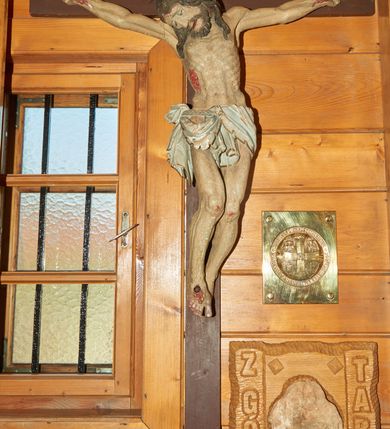 Zdjęcie nr 1: Pełnoplastyczna figura Chrystusa przybita do krzyża trzema gwoździami. Sylwetka postaci esowato wygięta, ukazana w lekkim zwisie, dłonie z zagiętymi palcami małym i serdecznym. Ciało wychudzone, z zaznaczonym układem kostnym, wyraźnym zwłaszcza w partii klatki piersiowej. Głowa pochylona, opadająca na prawe ramię.  Nogi lekko ugięte w kolanach, prawa stopa założona na lewą. Twarz o wyrazistych rysach, oczy przymknięte, nos  o prostym profilu, usta rozchylone, o lekko opadających kącikach. Twarz okolona krótką brodą oraz długimi włosami układającymi się w pojedyncze pasma opadające na ramiona. Perizonium udrapowane na podwójnym sznurze ze zwisem przy prawym biodrze. Karnacja ciała w szarokremowym odcieniu, włosy i broda ciemnobrązowe. Perizonium białe ze złotą lamówką na brzegach. Na stopach, prawym boku i dłoniach rany opracowane rzeźbiarsko z kroplami krwi, malowane czerwoną farbą. Krzyż nowy, prosty, malowany na kolor ciemnobrązowy.