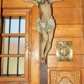 Zdjęcie nr 1: Pełnoplastyczna figura Chrystusa przybita do krzyża trzema gwoździami. Sylwetka postaci esowato wygięta, ukazana w lekkim zwisie, dłonie z zagiętymi palcami małym i serdecznym. Ciało wychudzone, z zaznaczonym układem kostnym, wyraźnym zwłaszcza w partii klatki piersiowej. Głowa pochylona, opadająca na prawe ramię.  Nogi lekko ugięte w kolanach, prawa stopa założona na lewą. Twarz o wyrazistych rysach, oczy przymknięte, nos  o prostym profilu, usta rozchylone, o lekko opadających kącikach. Twarz okolona krótką brodą oraz długimi włosami układającymi się w pojedyncze pasma opadające na ramiona. Perizonium udrapowane na podwójnym sznurze ze zwisem przy prawym biodrze. Karnacja ciała w szarokremowym odcieniu, włosy i broda ciemnobrązowe. Perizonium białe ze złotą lamówką na brzegach. Na stopach, prawym boku i dłoniach rany opracowane rzeźbiarsko z kroplami krwi, malowane czerwoną farbą. Krzyż nowy, prosty, malowany na kolor ciemnobrązowy.