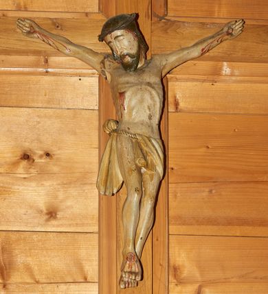 Zdjęcie nr 1: Rzeźba Chrystusa przybita do krzyża trzema gwoździami. Chrystus został ukazany w typie Cristo morto, w delikatnym zwisie, z głową skłonioną na prawe ramię, stopami założonymi prawa na lewą. Biodra ma przewiązane perizonium wiszącym na pojedynczym sznurze, przełożonym przez niego z lewej strony oraz zawiązanym na guza z prawej ze zwisem z prawej strony. Chrystus ma podłużną twarz, z wąskim nosem, zamkniętymi oczami, okoloną krótką i ciemnobrązową brodą; włosy długie i ciemnobrązowe, spływające na plecy. Na głowie ma założoną cienką koronę cierniową, splecioną z dwóch gałązek. Jego ciało jest szczupłe, o wyraźnie podkreślonej linii żeber i mostka, głęboko wciętej talii. Z ran spływają strużki krwi. Krzyż prosty, gładki, nad głową Chrytusa wisi titulus w formie poziomej banderoli z napisem „INRI”.


 
