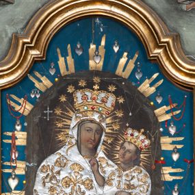 Zdjęcie nr 1: Obraz w kształcie stojącego prostokąta zamknięty łukiem wklęsło-wypukłym z uskokami, przedstawiający Matkę Boską z Dzieciątkiem. Maria została ukazana w półpostaci z Dzieciątkiem Jezus na lewym ręku, z jabłkiem w prawej dłoni (przysłoniętym sukienką), z głową delikatnie przechyloną na lewe ramię i wzrokiem skierowanym na widza. Twarz Marii o delikatnych rysach z drobnymi ustami, długim nosem i zarumienionymi policzkami. Dzieciątko ukazane jest w pozycji siedzącej, zwrócone trzy czwarte w prawo, prawą rączką czyni gest błogosławieństwa, lewą opiera na księdze. Twarz Dzieciątka owalna, pełna z długim nosem i półkolistymi łukami brwiowymi, policzki silnie zarumienione. Na postacie Marii i Dzieciątka nałożone są metalowe, złocone i srebrzone sukienki, dekorowane w motywy floralne, a także korony w typie zamkniętym. Karnacje blade. Całość ukazana jest na ciemnym tle, w którym wyróżniają się promieniste, złocone nimby wokół głów Marii i Dzieciątka. Obraz umieszczony na niebieskim tle, obwiedzionym wiązkami metalowych, złoconych promieni oraz zawieszonych wotów. Rama drewniana, profilowana złocona.