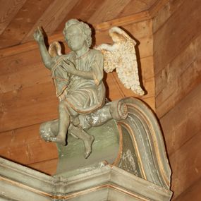 Zdjęcie nr 1: Dwie pełnoplastyczne figury siedzących na odcinkach przyczółka aniołów. Aniołek po prawej stronie wznosi prawą rękę ku górze, a lewą trzyma na wysokości piersi, nogi ukazane w ruchu, prawa noga wyciągniętą do przodu. Aniołek po lewej stronie ołtarza obie ręce wyciąga w swoją lewą stronę, a stopy ma skrzyżowane, kolana rozchylone na boki. Twarze pełne z dużymi ustami i krótkimi nosami, delikatnie zaznaczonymi oczami; włosy krótkie, ułożone w grube pukle. Postacie ubrane są w krótkie tuniki oraz zarzucone  na plecy płaszcze, szaty obwiedzione są złotą lamówką. Na plecach anioły mają duże, rozłożone skrzydła. Rzeźby w całości polichromowane są na kolor biały, skrzydła złocone.