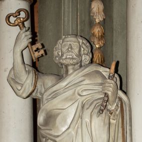 Zdjęcie nr 1: Rzeźba ścięta z tyłu, drążona, przedstawiająca św. Piotra. Święty ukazany jest w postawi stojącej, frontalnie  w delikatnym kontrapoście z prawą ręką uniesioną wysoko do góry, a lewą ugiętą w łokciu, w obu trzyma klucze. Twarz szeroka, okolona krótką brodą, nos długi, usta delikatnie rozchylone. Włosy średniej długości, sięgające za uszy, bujne. Święty ubrany jest w długą suknię z rękawami podwiniętymi do łokci oraz obszerny płaszcz zarzucony na lewe ramię i otaczający całą postać. Szaty na brzegach zdobione złotą lamówką. Rzeźba polichromowana na biało, atrybuty i brzeg szaty złocone.