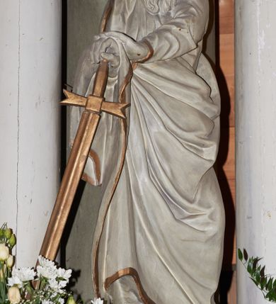 Zdjęcie nr 1: Rzeźba ścięta z tyłu, drążona, przedstawiająca św. Pawła. Święty ukazany jest w postawie stojącej z prawą nogą wysuniętą do przodu o esowato wygiętej sylwetce z dłońmi opartymi o miecz przy prawym boku. Twarz podłużna, okolona długą brodą, nos długi, głęboko osadzone oczy i wyraźnie zaznaczone kości policzkowe i łuki brwiowe. Włosy średniej długości, bujne. Święty ubrany jest w długą suknię oraz płaszcz zarzucony na prawe ramię i biegnący pod lewą ręką na prawe przedramię. Szaty na brzegach zdobione są złotą lamówką. Rzeźba polichromowana jest w całości na biało, atrybuty i brzeg szaty złocone. Rzeźba ustawiona jest na wysokim, prostopadłościennym cokole, zwężonym pośrodku, bogato profilowanym, polichromowanym na kolor jasnozielony.