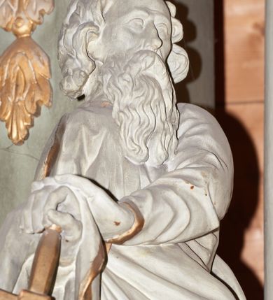 Zdjęcie nr 5: Rzeźba ścięta z tyłu, drążona, przedstawiająca św. Pawła. Święty ukazany jest w postawie stojącej z prawą nogą wysuniętą do przodu o esowato wygiętej sylwetce z dłońmi opartymi o miecz przy prawym boku. Twarz podłużna, okolona długą brodą, nos długi, głęboko osadzone oczy i wyraźnie zaznaczone kości policzkowe i łuki brwiowe. Włosy średniej długości, bujne. Święty ubrany jest w długą suknię oraz płaszcz zarzucony na prawe ramię i biegnący pod lewą ręką na prawe przedramię. Szaty na brzegach zdobione są złotą lamówką. Rzeźba polichromowana jest w całości na biało, atrybuty i brzeg szaty złocone. Rzeźba ustawiona jest na wysokim, prostopadłościennym cokole, zwężonym pośrodku, bogato profilowanym, polichromowanym na kolor jasnozielony.