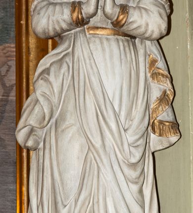 Zdjęcie nr 3: Rzeźba Matki Boskiej Niepokalanie Poczętej ustawiona frontalnie na globie ziemskim. Maria ma ręce złożone w geście modlitwy. Twarz owalna, pełna z dużym nosem i wyraźnie zaznaczonym podbródkiem. Włosy długie, bujne, opadające na ramiona i plecy. Maria ubrana jest w długą suknię, złoconą na brzegach rękawów i przewiązaną w talii złotym paskiem oraz płaszcz założony na prawe ramię o złoconej lamówce. Glob ziemski oplata wąż, malowany na złoto. Figura polichromowana na biało, detale złocone. Maria wokół głowy ma wieniec z dziewięciu gwiazd umieszczonych na metalowej obręczy.