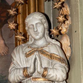 Zdjęcie nr 1: Rzeźba Matki Boskiej Niepokalanie Poczętej ustawiona frontalnie na globie ziemskim. Maria ma ręce złożone w geście modlitwy. Twarz owalna, pełna z dużym nosem i wyraźnie zaznaczonym podbródkiem. Włosy długie, bujne, opadające na ramiona i plecy. Maria ubrana jest w długą suknię, złoconą na brzegach rękawów i przewiązaną w talii złotym paskiem oraz płaszcz założony na prawe ramię o złoconej lamówce. Glob ziemski oplata wąż, malowany na złoto. Figura polichromowana na biało, detale złocone. Maria wokół głowy ma wieniec z dziewięciu gwiazd umieszczonych na metalowej obręczy.