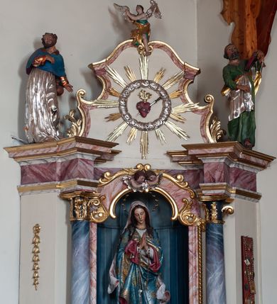 Zdjęcie nr 6: Ołtarz przyścienny, architektoniczny, jednoosiowy, jednokondygnacyjny ze zwieńczeniem. Ołtarz skrzyniowy, antepedium drewniane z wydzielonym polem w kształcie lezącego ośmioboku z dekoracją w formie marmoryzacji. Mensa drewniana, polichromowana. Retabulum ustawione na wysokim, zdwojonym cokole, ujęte parą kolumn korynckich wspierających przerwane, wyłamujące się belkowanie z profilowanym, silnie wysuniętym gzymsem. Zwieńczenie o formie wklęsło-wypukłej, flankowane spływami wolutowymi. Prostokątne pola cokołów kolumn dekorowane motywem roślinnym. Pole środkowe w formie prostokątnej wnęki zamkniętej fantazyjnym łukiem nadwieszonym ujętym stylizowanymi motywami roślinnymi, z dwoma uskrzydlonymi główkami aniołków pośrodku. Wewnątrz figura Matki Boskiej Niepokalanie Poczętej. W zwieńczeniu po bokach dwie pełnoplastyczne figury świętych (po lewej św. Jakub Większy z bukłakiem u boku), w polu motyw serca przeszytego mieczem boleści, ujętego okręgiem obłoków i promieni. Powyżej na gzymsie figurka anioła. Polichromia całości struktury w kolorze kremowym. Pola płycin, kolumny, elementy belkowania, obramienie niszy marmoryzowane. Detal architektoniczny i ornamenty złocone i srebrzone.  
