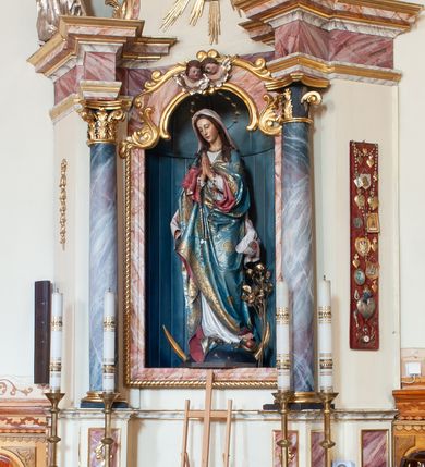 Zdjęcie nr 2: Ołtarz przyścienny, architektoniczny, jednoosiowy, jednokondygnacyjny ze zwieńczeniem. Ołtarz skrzyniowy, antepedium drewniane z wydzielonym polem w kształcie lezącego ośmioboku z dekoracją w formie marmoryzacji. Mensa drewniana, polichromowana. Retabulum ustawione na wysokim, zdwojonym cokole, ujęte parą kolumn korynckich wspierających przerwane, wyłamujące się belkowanie z profilowanym, silnie wysuniętym gzymsem. Zwieńczenie o formie wklęsło-wypukłej, flankowane spływami wolutowymi. Prostokątne pola cokołów kolumn dekorowane motywem roślinnym. Pole środkowe w formie prostokątnej wnęki zamkniętej fantazyjnym łukiem nadwieszonym ujętym stylizowanymi motywami roślinnymi, z dwoma uskrzydlonymi główkami aniołków pośrodku. Wewnątrz figura Matki Boskiej Niepokalanie Poczętej. W zwieńczeniu po bokach dwie pełnoplastyczne figury świętych (po lewej św. Jakub Większy z bukłakiem u boku), w polu motyw serca przeszytego mieczem boleści, ujętego okręgiem obłoków i promieni. Powyżej na gzymsie figurka anioła. Polichromia całości struktury w kolorze kremowym. Pola płycin, kolumny, elementy belkowania, obramienie niszy marmoryzowane. Detal architektoniczny i ornamenty złocone i srebrzone.  
