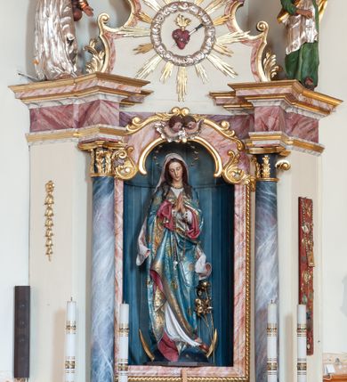 Zdjęcie nr 3: Ołtarz przyścienny, architektoniczny, jednoosiowy, jednokondygnacyjny ze zwieńczeniem. Ołtarz skrzyniowy, antepedium drewniane z wydzielonym polem w kształcie lezącego ośmioboku z dekoracją w formie marmoryzacji. Mensa drewniana, polichromowana. Retabulum ustawione na wysokim, zdwojonym cokole, ujęte parą kolumn korynckich wspierających przerwane, wyłamujące się belkowanie z profilowanym, silnie wysuniętym gzymsem. Zwieńczenie o formie wklęsło-wypukłej, flankowane spływami wolutowymi. Prostokątne pola cokołów kolumn dekorowane motywem roślinnym. Pole środkowe w formie prostokątnej wnęki zamkniętej fantazyjnym łukiem nadwieszonym ujętym stylizowanymi motywami roślinnymi, z dwoma uskrzydlonymi główkami aniołków pośrodku. Wewnątrz figura Matki Boskiej Niepokalanie Poczętej. W zwieńczeniu po bokach dwie pełnoplastyczne figury świętych (po lewej św. Jakub Większy z bukłakiem u boku), w polu motyw serca przeszytego mieczem boleści, ujętego okręgiem obłoków i promieni. Powyżej na gzymsie figurka anioła. Polichromia całości struktury w kolorze kremowym. Pola płycin, kolumny, elementy belkowania, obramienie niszy marmoryzowane. Detal architektoniczny i ornamenty złocone i srebrzone.  
