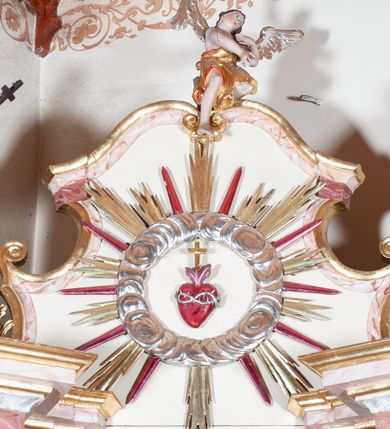 Zdjęcie nr 10: Ołtarz przyścienny, architektoniczny, jednoosiowy, jednokondygnacyjny. Mensa drewniana o formach wklęsło-wypukłych; na licu płycina w formie leżącego prostokąta o ściętych narożach wypełniona marmoryzacją. Tabernakulum dwudrzwiczkowe, zamknięte łukiem pełnym, ujęte dwiema  kolumienkami o kompozytowych kapitelach. W zwieńczeniu ażurowa, złocona dekoracja w formie przeciwstawnie ustawionego akantu z palmetą na osi. Na drzwiczkach płaskorzeźbione kłosy oraz winne grona. Retabulum na wysokim cokole ujęte ustawionymi ukośnie kolumnami o kompozytowych kapitelach i marmoryzowanych trzonach umiejscowionymi na wysokich postumentach (lica zdobione marmoryzowanymi płycinami  wypełnioymi rocaille'm). Podpory dźwigają odcinki pełnego, wyłamanego belkowania zwieńczonego wydatnym, silnie profilowanym gzymsem. Na belkowaniu, na osiach kolumn pełnoplastyczne figury niezidentyfikowanych świętych z krzyżem w ręku (z lewej, św. Jan Nepomucen?) oraz z księgą (z prawej). W polu centralnym nisza zamknięta u góry łukiem o falistym zarysie utworzonym przez dwie przeciwstawnie ustawione woluty. Nisza mieści pełnoplastyczną figurę Chrystusa z gorejącym sercem. Ponad nią, a osi dwie płaskorzeźbione uskrzydlone główki anielskie. Zwieńczenie o wolutowo wyciętych bokach zamknięte łukiem wklęsło-wypukłym. W polu płaskorzeźbione przedstawienie gorejącego serca w srebrzonym medalionie z obłoków oraz glorii promienistej o alternowanych promieniach. Powyżej na osi, pełnoplastyczna figura uskrzydlonego anioła. Po bokach wota i kampanule. Struktura malowana na kolor jasnobeżowy. Marmoryzacja w odcieniach różu. Ornamentyka oraz załamania profili architektonicznych złocone.