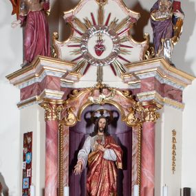 Zdjęcie nr 1: Ołtarz przyścienny, architektoniczny, jednoosiowy, jednokondygnacyjny. Mensa drewniana o formach wklęsło-wypukłych; na licu płycina w formie leżącego prostokąta o ściętych narożach wypełniona marmoryzacją. Tabernakulum dwudrzwiczkowe, zamknięte łukiem pełnym, ujęte dwiema  kolumienkami o kompozytowych kapitelach. W zwieńczeniu ażurowa, złocona dekoracja w formie przeciwstawnie ustawionego akantu z palmetą na osi. Na drzwiczkach płaskorzeźbione kłosy oraz winne grona. Retabulum na wysokim cokole ujęte ustawionymi ukośnie kolumnami o kompozytowych kapitelach i marmoryzowanych trzonach umiejscowionymi na wysokich postumentach (lica zdobione marmoryzowanymi płycinami  wypełnioymi rocaille&#039;m). Podpory dźwigają odcinki pełnego, wyłamanego belkowania zwieńczonego wydatnym, silnie profilowanym gzymsem. Na belkowaniu, na osiach kolumn pełnoplastyczne figury niezidentyfikowanych świętych z krzyżem w ręku (z lewej, św. Jan Nepomucen?) oraz z księgą (z prawej). W polu centralnym nisza zamknięta u góry łukiem o falistym zarysie utworzonym przez dwie przeciwstawnie ustawione woluty. Nisza mieści pełnoplastyczną figurę Chrystusa z gorejącym sercem. Ponad nią, a osi dwie płaskorzeźbione uskrzydlone główki anielskie. Zwieńczenie o wolutowo wyciętych bokach zamknięte łukiem wklęsło-wypukłym. W polu płaskorzeźbione przedstawienie gorejącego serca w srebrzonym medalionie z obłoków oraz glorii promienistej o alternowanych promieniach. Powyżej na osi, pełnoplastyczna figura uskrzydlonego anioła. Po bokach wota i kampanule. Struktura malowana na kolor jasnobeżowy. Marmoryzacja w odcieniach różu. Ornamentyka oraz załamania profili architektonicznych złocone.