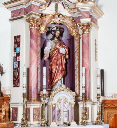 Zdjęcie nr 4: Ołtarz przyścienny, architektoniczny, jednoosiowy, jednokondygnacyjny. Mensa drewniana o formach wklęsło-wypukłych; na licu płycina w formie leżącego prostokąta o ściętych narożach wypełniona marmoryzacją. Tabernakulum dwudrzwiczkowe, zamknięte łukiem pełnym, ujęte dwiema  kolumienkami o kompozytowych kapitelach. W zwieńczeniu ażurowa, złocona dekoracja w formie przeciwstawnie ustawionego akantu z palmetą na osi. Na drzwiczkach płaskorzeźbione kłosy oraz winne grona. Retabulum na wysokim cokole ujęte ustawionymi ukośnie kolumnami o kompozytowych kapitelach i marmoryzowanych trzonach umiejscowionymi na wysokich postumentach (lica zdobione marmoryzowanymi płycinami  wypełnioymi rocaille&#039;m). Podpory dźwigają odcinki pełnego, wyłamanego belkowania zwieńczonego wydatnym, silnie profilowanym gzymsem. Na belkowaniu, na osiach kolumn pełnoplastyczne figury niezidentyfikowanych świętych z krzyżem w ręku (z lewej, św. Jan Nepomucen?) oraz z księgą (z prawej). W polu centralnym nisza zamknięta u góry łukiem o falistym zarysie utworzonym przez dwie przeciwstawnie ustawione woluty. Nisza mieści pełnoplastyczną figurę Chrystusa z gorejącym sercem. Ponad nią, a osi dwie płaskorzeźbione uskrzydlone główki anielskie. Zwieńczenie o wolutowo wyciętych bokach zamknięte łukiem wklęsło-wypukłym. W polu płaskorzeźbione przedstawienie gorejącego serca w srebrzonym medalionie z obłoków oraz glorii promienistej o alternowanych promieniach. Powyżej na osi, pełnoplastyczna figura uskrzydlonego anioła. Po bokach wota i kampanule. Struktura malowana na kolor jasnobeżowy. Marmoryzacja w odcieniach różu. Ornamentyka oraz załamania profili architektonicznych złocone.