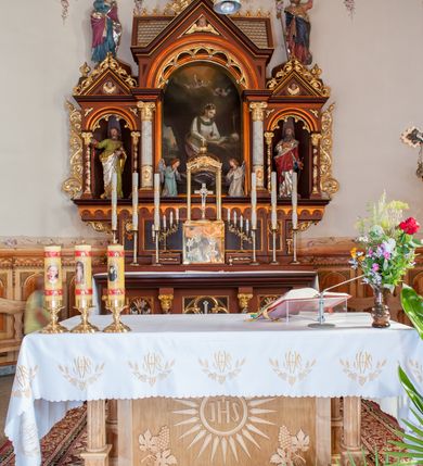 Zdjęcie nr 4: Ołtarz przyścienny, architektoniczny, trójosiowy. Mensa ołtarzowa skrzyniowa, prostopadłościenna z kamiennym portatylem, zamknięta profilowanym gzymsem podtrzymywanym przez cztery marmoryzowane kolumny. Antepedium dekorowane trzema płycinami: środkowa kwadratowa z krzyżem trójlistnym w czworoliściu, boczne  z aplikowanym motywem winorośli i kłosów zbóż. Retabulum ustawione na predelli, trójosiowe o półkoliście zamkniętych wnękach zakończonych trójkątnymi szczytami, w polu których uskrzydlone główki anielskie w medalionach. Wnęka środkowa wyższa i szersza zamknięta dwuspadowym daszkiem, ujęta parą kolumn kompozytowych wspierających odcinki gzymsu. Wewnątrz obraz z przedstawieniem  św. Rozalii. We wnękach bocznych pełnoplastyczne figury św. Piotra po lewej i św. Pawła po prawej stronie.  Nad wnęką środkową baldachim z figurą Chrystusa Zmartwychwstałego, po bokach pełnoplastyczne figury świętych. Predella dekorowana fryzem arkadkowym oraz płycinami z maswerkowaniem i rozetami, boki retabulum ujęte ażurowymi uszakami formowanymi z wici roślinnej. Półkoliste łuki wnęk zdobione arkadkami. Całość polichromowana na odcień ciemnobrązowy, detal architektoniczny i profilowania pomarańczowe oraz złocone. 
