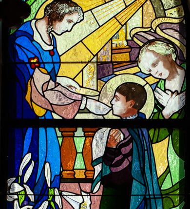 Zdjęcie nr 1: Witraż w kształcie stojącego prostokąta zamkniętego półkoliście z przedstawieniem św. Stanisława Kostki. Święty ukazany jako młody chłopiec, z lewego profilu, w pozycji klęczącej, w momencie przyjmowania Komunii Świętej z rąk stojącego naprzeciw niego Anioła. Ubrany jest w strój jezuity i niebieski płaszcz spływający na ziemię. Anioł udzielający Komunii ubrany jest w spodnią, bladoróżową szatę z długimi rękawami oraz wierzchnią ciemnoniebieską, z szerokimi, rozciętymi rękawami. Za postacią świętego widoczny drugi anioł ze złożonymi na piersiach rękami, ubrany w szatę w odcieniach zieleni. Scena ukazana na tle sumarycznie oddanej przestrzeni architektonicznej. U dołu, po lewej stronie gałązki białych lilii. W górnej partii witrażu łuk z malowaną dekoracją ornamentalną i snop światła padający na anioła. W dolnej części napisy, od lewej: „FUNDOWALI: / IGNACY I / JÓZEF / GAJNIAK”, pośrodku „św(ięty) STANISŁAWIE KOSTKO / MÓDL SIĘ ZA NAMI”, po prawej „JABŁONKA / ORAWSKA / 1938”.
