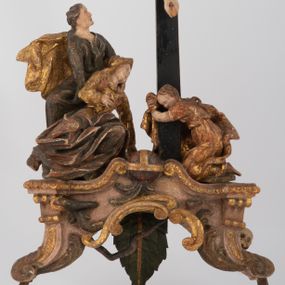 Zdjęcie nr 1: Rzeźbiarska grupa Ukrzyżowania z Matką Boską, św. Janem Ewangelistą i św. Marią Magdaleną ustawiona na cokole, wspartym na dwóch wolutowych nóżkach i trzeciej w formie liścia. Frontalna ścianka cokołu flankowana pilastrami i zamknięta gzymsem utworzonym z dwóch wolut, spiętych pośrodku kulą, dekorowanym perełkowaniem. Jego pole zdobione jest esownicami, palmami oraz niewielką rzeźbą węża gryzącego jabłko po lewej i czaszką po prawej stronie cokołu. Na cokole ustawiona grupa rzeźbiarska: nieco z prawej strony krucyfiks i św. Maria Magdalena, po lewej św. Jan Ewangelista i Matka Boska. Chrystus przybity do krzyża trzema gwoździami. Figura w dużym zwisie o układzie rąk bliskim literze „V”, sylwetka esowato wygięta, stopy ułożone w układzie prawa na lewą, głowa opuszczona na prawe ramię. Twarz okolona zarostem, włosy długie, spływające na prawe ramię, na głowie korona cierniowa oraz krzyżowy nimb promienisty, zachowany fragmentarycznie. Ciało wychudzone o plastycznie kształtowanej anatomii z podkreśloną muskulaturą i zaznaczonymi śladami męki. Perizonium w formie tkaniny przewiązanej sznurem, z odsłoniętym prawym biodrem oraz zwisem z tyłu. Krzyż gładki, pomalowany na czarno. Poniżej figura św. Marii Magdaleny ukazana w pozycji klęczącej, rękami obejmująca krzyż, ustawiona na niskim cokole. Święta widoczna z lewego profilu. Twarz szeroka, usta małe, oczy zamknięte, czoło wysokie, długie włosy opadają na plecy. Święta ubrana w długą suknię z krótkimi rękawami oraz obszerny płaszcz okrywający ją z prawego boku, którego jedną połę trzyma w dłoniach. Po lewej stronie kompozycji św. Jan Ewangelista podtrzymujący rękami mdlejącą Matkę Boską. Święty zwrócony delikatnie w lewo, z głową skierowaną w stronę krzyża. Twarz szeroka, nos długi i szeroki, oczy skierowane ku górze, usta wąskie, długie włosy opadają na plecy. Święty ubrany w długą suknię z długimi rękawami oraz płaszcz rozwiany za jego plecami. Poniżej Matka Boska, która opada bezwładnie, prawą rękę trzyma na piersi, lewą opuszcza w dół. Twarz szeroka z zamkniętymi oczami i małymi ustami. Ubrana w długą suknię z długimi rękawami, welon na głowie oraz płaszcz otulający nogi. Polichromia naturalistyczna w odsłoniętych partiach ciała, szaty i ornamenty na cokole złocone.
