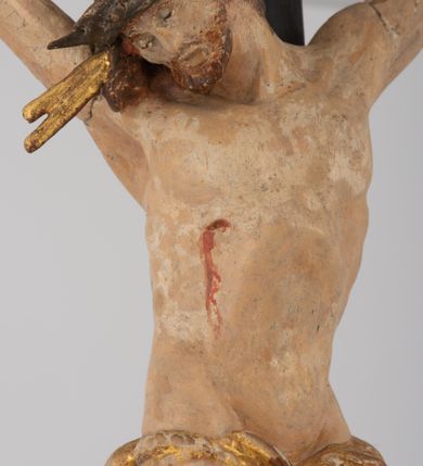 Zdjęcie nr 3: Rzeźbiarska grupa Ukrzyżowania z Matką Boską, św. Janem Ewangelistą i św. Marią Magdaleną ustawiona na cokole, wspartym na dwóch wolutowych nóżkach i trzeciej w formie liścia. Frontalna ścianka cokołu flankowana pilastrami i zamknięta gzymsem utworzonym z dwóch wolut, spiętych pośrodku kulą, dekorowanym perełkowaniem. Jego pole zdobione jest esownicami, palmami oraz niewielką rzeźbą węża gryzącego jabłko po lewej i czaszką po prawej stronie cokołu. Na cokole ustawiona grupa rzeźbiarska: nieco z prawej strony krucyfiks i św. Maria Magdalena, po lewej św. Jan Ewangelista i Matka Boska. Chrystus przybity do krzyża trzema gwoździami. Figura w dużym zwisie o układzie rąk bliskim literze „V”, sylwetka esowato wygięta, stopy ułożone w układzie prawa na lewą, głowa opuszczona na prawe ramię. Twarz okolona zarostem, włosy długie, spływające na prawe ramię, na głowie korona cierniowa oraz krzyżowy nimb promienisty, zachowany fragmentarycznie. Ciało wychudzone o plastycznie kształtowanej anatomii z podkreśloną muskulaturą i zaznaczonymi śladami męki. Perizonium w formie tkaniny przewiązanej sznurem, z odsłoniętym prawym biodrem oraz zwisem z tyłu. Krzyż gładki, pomalowany na czarno. Poniżej figura św. Marii Magdaleny ukazana w pozycji klęczącej, rękami obejmująca krzyż, ustawiona na niskim cokole. Święta widoczna z lewego profilu. Twarz szeroka, usta małe, oczy zamknięte, czoło wysokie, długie włosy opadają na plecy. Święta ubrana w długą suknię z krótkimi rękawami oraz obszerny płaszcz okrywający ją z prawego boku, którego jedną połę trzyma w dłoniach. Po lewej stronie kompozycji św. Jan Ewangelista podtrzymujący rękami mdlejącą Matkę Boską. Święty zwrócony delikatnie w lewo, z głową skierowaną w stronę krzyża. Twarz szeroka, nos długi i szeroki, oczy skierowane ku górze, usta wąskie, długie włosy opadają na plecy. Święty ubrany w długą suknię z długimi rękawami oraz płaszcz rozwiany za jego plecami. Poniżej Matka Boska, która opada bezwładnie, prawą rękę trzyma na piersi, lewą opuszcza w dół. Twarz szeroka z zamkniętymi oczami i małymi ustami. Ubrana w długą suknię z długimi rękawami, welon na głowie oraz płaszcz otulający nogi. Polichromia naturalistyczna w odsłoniętych partiach ciała, szaty i ornamenty na cokole złocone.
