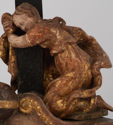 Zdjęcie nr 8: Rzeźbiarska grupa Ukrzyżowania z Matką Boską, św. Janem Ewangelistą i św. Marią Magdaleną ustawiona na cokole, wspartym na dwóch wolutowych nóżkach i trzeciej w formie liścia. Frontalna ścianka cokołu flankowana pilastrami i zamknięta gzymsem utworzonym z dwóch wolut, spiętych pośrodku kulą, dekorowanym perełkowaniem. Jego pole zdobione jest esownicami, palmami oraz niewielką rzeźbą węża gryzącego jabłko po lewej i czaszką po prawej stronie cokołu. Na cokole ustawiona grupa rzeźbiarska: nieco z prawej strony krucyfiks i św. Maria Magdalena, po lewej św. Jan Ewangelista i Matka Boska. Chrystus przybity do krzyża trzema gwoździami. Figura w dużym zwisie o układzie rąk bliskim literze „V”, sylwetka esowato wygięta, stopy ułożone w układzie prawa na lewą, głowa opuszczona na prawe ramię. Twarz okolona zarostem, włosy długie, spływające na prawe ramię, na głowie korona cierniowa oraz krzyżowy nimb promienisty, zachowany fragmentarycznie. Ciało wychudzone o plastycznie kształtowanej anatomii z podkreśloną muskulaturą i zaznaczonymi śladami męki. Perizonium w formie tkaniny przewiązanej sznurem, z odsłoniętym prawym biodrem oraz zwisem z tyłu. Krzyż gładki, pomalowany na czarno. Poniżej figura św. Marii Magdaleny ukazana w pozycji klęczącej, rękami obejmująca krzyż, ustawiona na niskim cokole. Święta widoczna z lewego profilu. Twarz szeroka, usta małe, oczy zamknięte, czoło wysokie, długie włosy opadają na plecy. Święta ubrana w długą suknię z krótkimi rękawami oraz obszerny płaszcz okrywający ją z prawego boku, którego jedną połę trzyma w dłoniach. Po lewej stronie kompozycji św. Jan Ewangelista podtrzymujący rękami mdlejącą Matkę Boską. Święty zwrócony delikatnie w lewo, z głową skierowaną w stronę krzyża. Twarz szeroka, nos długi i szeroki, oczy skierowane ku górze, usta wąskie, długie włosy opadają na plecy. Święty ubrany w długą suknię z długimi rękawami oraz płaszcz rozwiany za jego plecami. Poniżej Matka Boska, która opada bezwładnie, prawą rękę trzyma na piersi, lewą opuszcza w dół. Twarz szeroka z zamkniętymi oczami i małymi ustami. Ubrana w długą suknię z długimi rękawami, welon na głowie oraz płaszcz otulający nogi. Polichromia naturalistyczna w odsłoniętych partiach ciała, szaty i ornamenty na cokole złocone.
