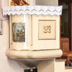 Zdjęcie nr 1: Ambona przyścienna, wisząca, z dostępem z prawej strony w postaci jednobiegowych schodów. Kosz czworoboczny, na planie kwadratu, o wypukłej ściance bocznej, z półwałkiem u dołu i podwieszoną szyszką. Na ściance frontowej kwadratowa płycina ze stylizowaną rozetą w polu. Na lewej ściance bocznej żłobkowanie i płaskorzeźba przedstawiająca Siewcę. Zaplecek w kształcie wydłużonego prostokąta, flankowany dwoma pilastrami, zamknięty profilowanym gzymsem. W polu dwie pionowe płyciny, górna zamknięta łukiem półkolistym, zdobione pojedynczymi motywami ornamentalnymi. Baldachim na planie kwadratu o ściętych narożach, na brzegach zdobiony lambrekinem. Na szczycie krzyż i otwarta księga z monogramami Chrystusa i Marii, ustawione na tle promienistej glorii i obłoków. Na podniebieniu baldachimu gołębica Ducha Świętego na tle promienistej glorii, złożonej z wiązek promieni o nierównej długości. Struktura polichromowana na kolor beżowy, detale jasnozielone i srebrzone, ornamentyka i profilowania złocone. Płaskorzeźba w kształcie poziomego prostokąta, ujęta złoconą ramą. Pośrodku kompozycji mężczyzna zwrócony trzy czwarte w lewo, lewą ręką przytrzymuje płachtę z ziarnem, prawą sieje zboże na zaorane pole. Twarz szeroka, okolona brodą, włosy długie i bujne, opadające na plecy. Ubrany w spodnie górali orawskich, krótką sukmanę oraz torbę skórzaną przy pasku. Po lewej stronie obrazu umieszczone wysokie drzewo oraz ptaki wydziobujące ziarno, po prawej woły zaprzęgnięte do pługa oraz krzyż na wysokim pagórku. W oddali pejzaż wiejski, powyżej błękitne niebo. Kolorystyka ciepła, stonowana. Na kamieniu, po lewej stronie data „1869”.
