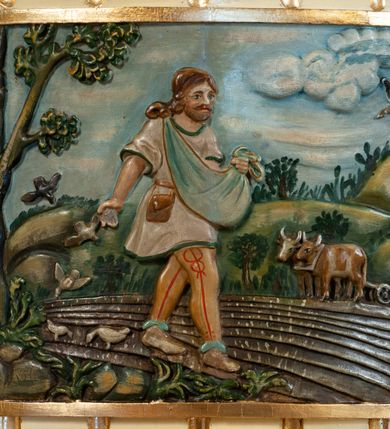 Zdjęcie nr 2: Ambona przyścienna, wisząca, z dostępem z prawej strony w postaci jednobiegowych schodów. Kosz czworoboczny, na planie kwadratu, o wypukłej ściance bocznej, z półwałkiem u dołu i podwieszoną szyszką. Na ściance frontowej kwadratowa płycina ze stylizowaną rozetą w polu. Na lewej ściance bocznej żłobkowanie i płaskorzeźba przedstawiająca Siewcę. Zaplecek w kształcie wydłużonego prostokąta, flankowany dwoma pilastrami, zamknięty profilowanym gzymsem. W polu dwie pionowe płyciny, górna zamknięta łukiem półkolistym, zdobione pojedynczymi motywami ornamentalnymi. Baldachim na planie kwadratu o ściętych narożach, na brzegach zdobiony lambrekinem. Na szczycie krzyż i otwarta księga z monogramami Chrystusa i Marii, ustawione na tle promienistej glorii i obłoków. Na podniebieniu baldachimu gołębica Ducha Świętego na tle promienistej glorii, złożonej z wiązek promieni o nierównej długości. Struktura polichromowana na kolor beżowy, detale jasnozielone i srebrzone, ornamentyka i profilowania złocone. Płaskorzeźba w kształcie poziomego prostokąta, ujęta złoconą ramą. Pośrodku kompozycji mężczyzna zwrócony trzy czwarte w lewo, lewą ręką przytrzymuje płachtę z ziarnem, prawą sieje zboże na zaorane pole. Twarz szeroka, okolona brodą, włosy długie i bujne, opadające na plecy. Ubrany w spodnie górali orawskich, krótką sukmanę oraz torbę skórzaną przy pasku. Po lewej stronie obrazu umieszczone wysokie drzewo oraz ptaki wydziobujące ziarno, po prawej woły zaprzęgnięte do pługa oraz krzyż na wysokim pagórku. W oddali pejzaż wiejski, powyżej błękitne niebo. Kolorystyka ciepła, stonowana. Na kamieniu, po lewej stronie data „1869”.
