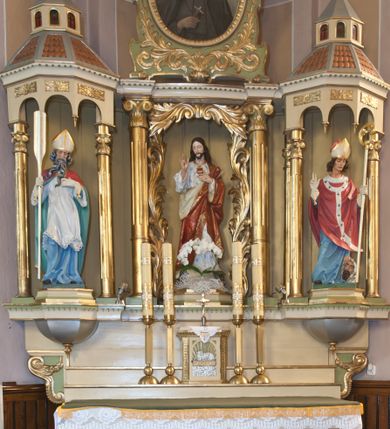 Zdjęcie nr 1: Ołtarz przyścienny, architektoniczny, trójosiowy, jednokondygnacyjny ze zwieńczeniem. Ołtarz skrzyniowy, sarkofagowy, z kamiennym portatylem. Mensa wklęsło-wypukła, z wydzielonym polem, pośrodku którego, ujęte okrągłą ramą płaskorzeźbione, polichromowane gorejące serce. Tabernakulum w formie prostopadłościennej skrzynki, ustawione na niskim cokole, ujęte parą lizen zdobionych cekinami, zamknięte profilowanych gzymsem. Drzwiczki dekorowane płyciną w kształcie stojącego prostokąta, zamkniętego łukiem półkolistym, w polu z płaskorzeźbionym barankiem siedzącym na księdze na zielonym tle, w dolnej części kompozycji srebrne obłoki, w górnej złote promienie. Retabulum ustawione na wysokim cokole, kształtowanym schodkowo, po bokach ujętym małymi spływami wolutowymi. Osie boczne retabulum w formie ażurowych, architektonicznych tempiett, o profilowanych wielobocznych podstawach z pięciobocznym podwieszeniem. Baldachimy, wsparte na parze kolumn, kształtowane są na wzór architektonicznych dachów, z wycięciem arkadkowym u dołu oraz ze zwieńczeniem w formie wielobocznej latarni zakończonej kwiatonem. W niszy po lewej figura św. Wojciecha, a po prawej św. Stanisława. Część środkowa retabulum flankowana parą kolumn wspierających wyłamane pośrodku niepełne belkowanie. W polu obraz rzeźba Najświętsze Serce Jezusa, dookoła dekorowana bujnym ornamentem akantowym. Zwieńczenie w formie owalu ujętego dekoracyjną ramą z obrazem św. Andrzeja Boboli. U szczytu rzeźbiona, uskrzydlona główka aniołka i łaciński krzyż. Polichromia w kolorze jasnobeżowym, detale zielone, profilowania i ornamentyka złocone.