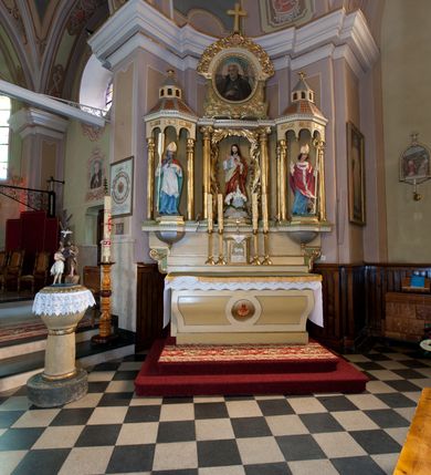 Zdjęcie nr 2: Ołtarz przyścienny, architektoniczny, trójosiowy, jednokondygnacyjny ze zwieńczeniem. Ołtarz skrzyniowy, sarkofagowy, z kamiennym portatylem. Mensa wklęsło-wypukła, z wydzielonym polem, pośrodku którego, ujęte okrągłą ramą płaskorzeźbione, polichromowane gorejące serce. Tabernakulum w formie prostopadłościennej skrzynki, ustawione na niskim cokole, ujęte parą lizen zdobionych cekinami, zamknięte profilowanych gzymsem. Drzwiczki dekorowane płyciną w kształcie stojącego prostokąta, zamkniętego łukiem półkolistym, w polu z płaskorzeźbionym barankiem siedzącym na księdze na zielonym tle, w dolnej części kompozycji srebrne obłoki, w górnej złote promienie. Retabulum ustawione na wysokim cokole, kształtowanym schodkowo, po bokach ujętym małymi spływami wolutowymi. Osie boczne retabulum w formie ażurowych, architektonicznych tempiett, o profilowanych wielobocznych podstawach z pięciobocznym podwieszeniem. Baldachimy, wsparte na parze kolumn, kształtowane są na wzór architektonicznych dachów, z wycięciem arkadkowym u dołu oraz ze zwieńczeniem w formie wielobocznej latarni zakończonej kwiatonem. W niszy po lewej figura św. Wojciecha, a po prawej św. Stanisława. Część środkowa retabulum flankowana parą kolumn wspierających wyłamane pośrodku niepełne belkowanie. W polu obraz rzeźba Najświętsze Serce Jezusa, dookoła dekorowana bujnym ornamentem akantowym. Zwieńczenie w formie owalu ujętego dekoracyjną ramą z obrazem św. Andrzeja Boboli. U szczytu rzeźbiona, uskrzydlona główka aniołka i łaciński krzyż. Polichromia w kolorze jasnobeżowym, detale zielone, profilowania i ornamentyka złocone.