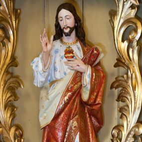 Zdjęcie nr 1: Rzeźba pełnoplastyczna, wolnostojąca, ustawiona na niskim prostopadłościennym cokole. Chrystus ukazany w całej postaci, stojący w delikatnym kontrapoście, prawą ręką czyni gest błogosławieństwa, lewą wskazuje na gorejące na piersi serce. Głowa delikatnie skłoniona w dół i w prawą stronę. Twarz podłużna z długim i wąskim nosem, okolona krótką, ciemną brodą, rozdzieloną na dwa krótkie pukle. Włosy długie, ciemnobrązowe, z przedziałkiem pośrodku, opadające na plecy i lewe ramię. Chrystus ubrany jest w długą białą suknię, obszytą na brzegach złotą lamówką, zdobioną w niebieskie kwiaty i złote, małe gwiazdki. Suknia przewiązana w talii złotym paskiem. Na plecy i przez lewe ramię ma założony czerwony płaszcz o białej podszewce, bogato zdobiony stylizowanymi kwiatami, a na podszewce małymi krzyżykami. Na dłoniach widoczne ślady męki, a na piersi gorejące serce, oplecione koroną cierniową, z zatkniętym u góry krzyżykiem. Polichromia w odsłoniętych partiach ciała naturalistyczna. 