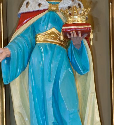 Zdjęcie nr 1: Figura św. Kazimierza Jagiellończyka ustawiona na niskim cokole. Święty ukazany w pozycji stojącej, frontalnie, w lekkim kontrapoście, w lewej dłoni trzyma koronę otwartą ułożoną na czerwonej poduszce, prawą wysuwa do przodu. Twarz szeroka o ostrych rysach, dużych i głęboko osadzonych oczach, długim i szerokim nosie, bez zarostu. Włosy długie, z przedziałkiem pośrodku, opadające bujnymi falami na plecy. Święty jest ubrany w długą, błękitną suknię z szerokimi rękawami, ze złotym obszyciem wokół szyi, spiętą w talii złotym pasem. Spod sukni widoczne złocone trzewiki zakończone kwadratowymi noskami. Na plecy zarzucony długi, czerwony płaszcz, z jasnożółtą podszewką, z gronostajową pelerynką, spięty na piersiach złotą fibulą. Polichromia w odsłoniętych partiach ciała naturalistyczna, detale złocone.