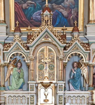 Zdjęcie nr 4: Nastawa ołtarzowa architektoniczna, trójosiowa, jednokondygnacyjna z predellą, ze zwieńczeniem, na cokole. Cokół dekorowany płycinami z arkadami, w których znajdują się biforia. Mensa kamienna z portatylem. Antepedium z płaskorzeźbioną sceną Ostatniej Wieczerzy w niszy ujętej arkadkami. Scena flankowana dwiema płycinami z ornamentem roślinnym, ujęta kolumnami w ściętych narożach. Tabernakulum trójosiowe w formie prostopadłościennej skrzynki z tronem wystawienia, rozbudowanym architektonicznie, ustawionym na niskim cokole dekorowanym arkadowaniem. Pośrodku tron wystawienia flankowany odwróconą parą odrzwi z figurami aniołów, z monogramem IHS w polu na białym tle, zamknięty trójkątnym przyczółkiem, na szczycie kopuła wsparta na wąskich kolumienkach zwieńczona krzyżykiem. W osiach bocznych arkady z figurami klęczących aniołów, zamknięte zwieńczeniem analogicznym jak w osi środkowej. Predella w formie arkadek z płaskorzeźbionymi scenami, od lewej: Narodzenie Chrystusa, Nauczanie w świątyni, Chrystus wśród dzieci i Zmartwychwstanie. Arkady predelli dekorowane krenelażem, w przyłuczach zdobione ornamentem roślinnym. Oś środkowa nastawy ołtarzowej ujęta dwiema parami kolumn dźwigającymi fryz i gzyms, na których opiera się półokrągły łuk flankowany przez dwie nisze z płaskorzeźbami aniołów. W polu środkowym obraz Przemienienie Pańskie. Trzony kolumn zdobione festonami. Osie boczne niższe, w formie arkad opartych na kolumnach, w których znajdują się figury po lewej św. Cyryla, a po prawej św. Metodego. Arkady dźwigają gzyms, na którym stoją figury, po lewej św. Agnieszki, a po prawej św. Elżbiety Węgierskiej. Zwieńczenie w formie medalionu z płaskorzeźbą Boga Ojca wśród obłoków z gołębicą Ducha Świętego. Całość obwiedziona astwerkiem. We fryzie ornament roślinno-geometryczny. Łuk pola obrazowego dekorowany palmetami, w przyłuczach ornament roślinny. Struktura polichromowana na kolor beżowy, detale na kolor jasnoszary i zielony, ornamentyka i detale złocone. 
