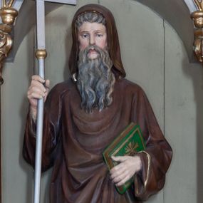 Zdjęcie nr 1: Rzeźba pełnoplastyczna przedstawiająca św. Cyryla, ustawiona na niskim cokole. Figura ustawiona frontalnie, w lewej ręce trzyma księgę, w prawej krzyż. Twarz pociągła, długi i szeroki nos, oczy skierowane na wprost, okolona bujną, siwą i długą brodą. Święty jest ubrany w brązową togę filozofa z długimi rękawami i kapturem założonym na głowę, obwiedzioną na brzegach stylizowaną wicią roślinną, pod spodem ma białą, długą suknię. Księga w zielonej obwolucie, z krzyżykiem greckim na okładce. Polichromia naturalistyczna w odsłoniętych partiach ciała, detale złocone i srebrzone.
