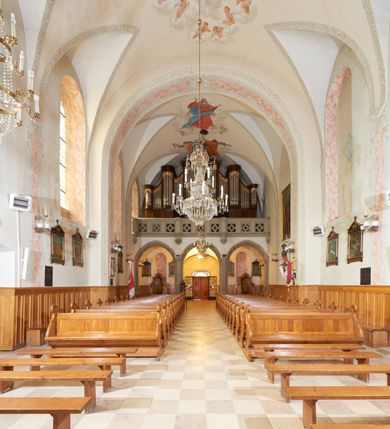 Zdjęcie nr 14: Kościół orientowany, murowany z cegły i kamienia, jednonawowy, na rzucie wydłużonego prostokąta z prezbiterium zamkniętym trójbocznie, wieżą na osi, zakrystią przy północnej ścianie prezbiterium, kruchtą przy południowej ścianie nawy i kaplicą od północy. Nawa pięcioprzęsłowa, ściany gładkie, sklepienie kolebkowe z lunetami, gurt między drugim, a trzecim przęsłem, pięć okien po stronie południowej, po północnej blendy odpowiadające wielkością i kształtem przeciwległym otworom okiennym. Prezbiterium oddzielone ścianą tęczową przeprutą łukiem o kształcie lekko zaostrzonym, dwuprzęsłowe, o sklepieniu krzyżowym, z dwoma ostrołukowymi oknami w ścianie południowej; zakrystia o sklepieniu sieciowym/gwiaździstym. Od zachodu chór wsparty arkadami z łukami o profilu lekko zaostrzonym, z balustradą zdobioną motywem rombu wypełnionego czworoliściem. Pod chórem skarbiec. Wejście główne od zachodu, boczne od południa z kruchtą (w nim kamienny portal z 1673 roku), kolejne od zakrystii, między zakrystią, a prezbiterium gotycki ostrołukowy portal z żelaznymi drzwiami z kratownicą rombową. 
Fasada wieżowa, z wejściem na osi po czterech stopniach. Przedsionek zwieńczony trójkątnym przyczółkiem z zatkniętym na szczycie krzyżem łacińskim. Drzwi zamknięte półkoliście, ponad nimi płaskorzeźba z przedstawieniem głowy Chrystusa otoczonej winną latoroślą. 
Wieża trójkondygnacyjna, zwieńczona trójkątnym przyczółkiem; w dolnej kondygnacji okulus, w środkowej okno zamknięte półkoliście, w ostatniej zegar w niszy powtarzającej kształt okna poniżej. 
Bryła rozczłonkowana; całość budynku obiega cokół, fragmentami kamienny, elewacje boczne oraz prezbiterium wsparte przyporami. Trzy przęsła nawy głównej otynkowane, reszta z cegły. Dachy dwuspadowe, nad pierwszymi dwoma przęsłami nawy niższy niż nad pozostałymi. Nad czwartym przęsłem nawy wieloboczna wieżyczka na sygnaturkę przepruta arkadami, przykryta dachem ostrosłupowym zakończonym kulą z krzyżem łacińskim.  
Do najcenniejszego wyposażenia kościoła należą: ołtarz główny z obrazem Ukrzyżowanego Chrystusa pędzla Jana Triciusa oraz słynący cudami obraz Matki Boskiej w ołtarzu bocznym. 
