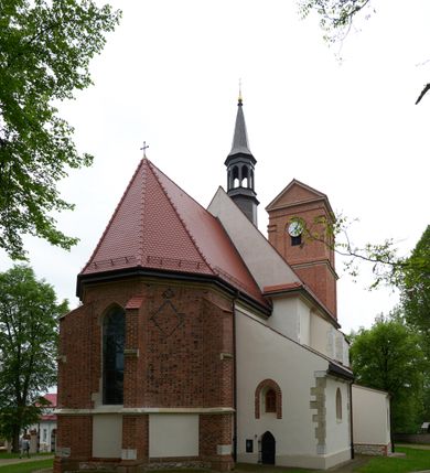 Zdjęcie nr 9: Kościół orientowany, murowany z cegły i kamienia, jednonawowy, na rzucie wydłużonego prostokąta z prezbiterium zamkniętym trójbocznie, wieżą na osi, zakrystią przy północnej ścianie prezbiterium, kruchtą przy południowej ścianie nawy i kaplicą od północy. Nawa pięcioprzęsłowa, ściany gładkie, sklepienie kolebkowe z lunetami, gurt między drugim, a trzecim przęsłem, pięć okien po stronie południowej, po północnej blendy odpowiadające wielkością i kształtem przeciwległym otworom okiennym. Prezbiterium oddzielone ścianą tęczową przeprutą łukiem o kształcie lekko zaostrzonym, dwuprzęsłowe, o sklepieniu krzyżowym, z dwoma ostrołukowymi oknami w ścianie południowej; zakrystia o sklepieniu sieciowym/gwiaździstym. Od zachodu chór wsparty arkadami z łukami o profilu lekko zaostrzonym, z balustradą zdobioną motywem rombu wypełnionego czworoliściem. Pod chórem skarbiec. Wejście główne od zachodu, boczne od południa z kruchtą (w nim kamienny portal z 1673 roku), kolejne od zakrystii, między zakrystią, a prezbiterium gotycki ostrołukowy portal z żelaznymi drzwiami z kratownicą rombową. 
Fasada wieżowa, z wejściem na osi po czterech stopniach. Przedsionek zwieńczony trójkątnym przyczółkiem z zatkniętym na szczycie krzyżem łacińskim. Drzwi zamknięte półkoliście, ponad nimi płaskorzeźba z przedstawieniem głowy Chrystusa otoczonej winną latoroślą. 
Wieża trójkondygnacyjna, zwieńczona trójkątnym przyczółkiem; w dolnej kondygnacji okulus, w środkowej okno zamknięte półkoliście, w ostatniej zegar w niszy powtarzającej kształt okna poniżej. 
Bryła rozczłonkowana; całość budynku obiega cokół, fragmentami kamienny, elewacje boczne oraz prezbiterium wsparte przyporami. Trzy przęsła nawy głównej otynkowane, reszta z cegły. Dachy dwuspadowe, nad pierwszymi dwoma przęsłami nawy niższy niż nad pozostałymi. Nad czwartym przęsłem nawy wieloboczna wieżyczka na sygnaturkę przepruta arkadami, przykryta dachem ostrosłupowym zakończonym kulą z krzyżem łacińskim.  
Do najcenniejszego wyposażenia kościoła należą: ołtarz główny z obrazem Ukrzyżowanego Chrystusa pędzla Jana Triciusa oraz słynący cudami obraz Matki Boskiej w ołtarzu bocznym. 
