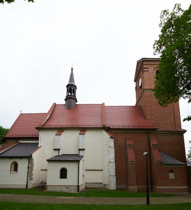 Zdjęcie nr 8: Kościół orientowany, murowany z cegły i kamienia, jednonawowy, na rzucie wydłużonego prostokąta z prezbiterium zamkniętym trójbocznie, wieżą na osi, zakrystią przy północnej ścianie prezbiterium, kruchtą przy południowej ścianie nawy i kaplicą od północy. Nawa pięcioprzęsłowa, ściany gładkie, sklepienie kolebkowe z lunetami, gurt między drugim, a trzecim przęsłem, pięć okien po stronie południowej, po północnej blendy odpowiadające wielkością i kształtem przeciwległym otworom okiennym. Prezbiterium oddzielone ścianą tęczową przeprutą łukiem o kształcie lekko zaostrzonym, dwuprzęsłowe, o sklepieniu krzyżowym, z dwoma ostrołukowymi oknami w ścianie południowej; zakrystia o sklepieniu sieciowym/gwiaździstym. Od zachodu chór wsparty arkadami z łukami o profilu lekko zaostrzonym, z balustradą zdobioną motywem rombu wypełnionego czworoliściem. Pod chórem skarbiec. Wejście główne od zachodu, boczne od południa z kruchtą (w nim kamienny portal z 1673 roku), kolejne od zakrystii, między zakrystią, a prezbiterium gotycki ostrołukowy portal z żelaznymi drzwiami z kratownicą rombową. 
Fasada wieżowa, z wejściem na osi po czterech stopniach. Przedsionek zwieńczony trójkątnym przyczółkiem z zatkniętym na szczycie krzyżem łacińskim. Drzwi zamknięte półkoliście, ponad nimi płaskorzeźba z przedstawieniem głowy Chrystusa otoczonej winną latoroślą. 
Wieża trójkondygnacyjna, zwieńczona trójkątnym przyczółkiem; w dolnej kondygnacji okulus, w środkowej okno zamknięte półkoliście, w ostatniej zegar w niszy powtarzającej kształt okna poniżej. 
Bryła rozczłonkowana; całość budynku obiega cokół, fragmentami kamienny, elewacje boczne oraz prezbiterium wsparte przyporami. Trzy przęsła nawy głównej otynkowane, reszta z cegły. Dachy dwuspadowe, nad pierwszymi dwoma przęsłami nawy niższy niż nad pozostałymi. Nad czwartym przęsłem nawy wieloboczna wieżyczka na sygnaturkę przepruta arkadami, przykryta dachem ostrosłupowym zakończonym kulą z krzyżem łacińskim.  
Do najcenniejszego wyposażenia kościoła należą: ołtarz główny z obrazem Ukrzyżowanego Chrystusa pędzla Jana Triciusa oraz słynący cudami obraz Matki Boskiej w ołtarzu bocznym. 
