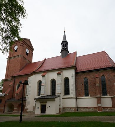 Zdjęcie nr 2: Kościół orientowany, murowany z cegły i kamienia, jednonawowy, na rzucie wydłużonego prostokąta z prezbiterium zamkniętym trójbocznie, wieżą na osi, zakrystią przy północnej ścianie prezbiterium, kruchtą przy południowej ścianie nawy i kaplicą od północy. Nawa pięcioprzęsłowa, ściany gładkie, sklepienie kolebkowe z lunetami, gurt między drugim, a trzecim przęsłem, pięć okien po stronie południowej, po północnej blendy odpowiadające wielkością i kształtem przeciwległym otworom okiennym. Prezbiterium oddzielone ścianą tęczową przeprutą łukiem o kształcie lekko zaostrzonym, dwuprzęsłowe, o sklepieniu krzyżowym, z dwoma ostrołukowymi oknami w ścianie południowej; zakrystia o sklepieniu sieciowym/gwiaździstym. Od zachodu chór wsparty arkadami z łukami o profilu lekko zaostrzonym, z balustradą zdobioną motywem rombu wypełnionego czworoliściem. Pod chórem skarbiec. Wejście główne od zachodu, boczne od południa z kruchtą (w nim kamienny portal z 1673 roku), kolejne od zakrystii, między zakrystią, a prezbiterium gotycki ostrołukowy portal z żelaznymi drzwiami z kratownicą rombową. 
Fasada wieżowa, z wejściem na osi po czterech stopniach. Przedsionek zwieńczony trójkątnym przyczółkiem z zatkniętym na szczycie krzyżem łacińskim. Drzwi zamknięte półkoliście, ponad nimi płaskorzeźba z przedstawieniem głowy Chrystusa otoczonej winną latoroślą. 
Wieża trójkondygnacyjna, zwieńczona trójkątnym przyczółkiem; w dolnej kondygnacji okulus, w środkowej okno zamknięte półkoliście, w ostatniej zegar w niszy powtarzającej kształt okna poniżej. 
Bryła rozczłonkowana; całość budynku obiega cokół, fragmentami kamienny, elewacje boczne oraz prezbiterium wsparte przyporami. Trzy przęsła nawy głównej otynkowane, reszta z cegły. Dachy dwuspadowe, nad pierwszymi dwoma przęsłami nawy niższy niż nad pozostałymi. Nad czwartym przęsłem nawy wieloboczna wieżyczka na sygnaturkę przepruta arkadami, przykryta dachem ostrosłupowym zakończonym kulą z krzyżem łacińskim.  
Do najcenniejszego wyposażenia kościoła należą: ołtarz główny z obrazem Ukrzyżowanego Chrystusa pędzla Jana Triciusa oraz słynący cudami obraz Matki Boskiej w ołtarzu bocznym. 
