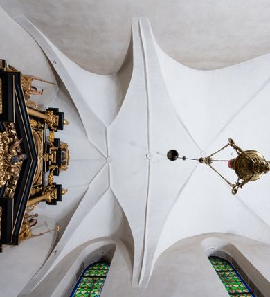 Zdjęcie nr 3: Kościół orientowany, murowany z cegły i kamienia, jednonawowy, na rzucie wydłużonego prostokąta z prezbiterium zamkniętym trójbocznie, wieżą na osi, zakrystią przy północnej ścianie prezbiterium, kruchtą przy południowej ścianie nawy i kaplicą od północy. Nawa pięcioprzęsłowa, ściany gładkie, sklepienie kolebkowe z lunetami, gurt między drugim, a trzecim przęsłem, pięć okien po stronie południowej, po północnej blendy odpowiadające wielkością i kształtem przeciwległym otworom okiennym. Prezbiterium oddzielone ścianą tęczową przeprutą łukiem o kształcie lekko zaostrzonym, dwuprzęsłowe, o sklepieniu krzyżowym, z dwoma ostrołukowymi oknami w ścianie południowej; zakrystia o sklepieniu sieciowym/gwiaździstym. Od zachodu chór wsparty arkadami z łukami o profilu lekko zaostrzonym, z balustradą zdobioną motywem rombu wypełnionego czworoliściem. Pod chórem skarbiec. Wejście główne od zachodu, boczne od południa z kruchtą (w nim kamienny portal z 1673 roku), kolejne od zakrystii, między zakrystią, a prezbiterium gotycki ostrołukowy portal z żelaznymi drzwiami z kratownicą rombową. 
Fasada wieżowa, z wejściem na osi po czterech stopniach. Przedsionek zwieńczony trójkątnym przyczółkiem z zatkniętym na szczycie krzyżem łacińskim. Drzwi zamknięte półkoliście, ponad nimi płaskorzeźba z przedstawieniem głowy Chrystusa otoczonej winną latoroślą. 
Wieża trójkondygnacyjna, zwieńczona trójkątnym przyczółkiem; w dolnej kondygnacji okulus, w środkowej okno zamknięte półkoliście, w ostatniej zegar w niszy powtarzającej kształt okna poniżej. 
Bryła rozczłonkowana; całość budynku obiega cokół, fragmentami kamienny, elewacje boczne oraz prezbiterium wsparte przyporami. Trzy przęsła nawy głównej otynkowane, reszta z cegły. Dachy dwuspadowe, nad pierwszymi dwoma przęsłami nawy niższy niż nad pozostałymi. Nad czwartym przęsłem nawy wieloboczna wieżyczka na sygnaturkę przepruta arkadami, przykryta dachem ostrosłupowym zakończonym kulą z krzyżem łacińskim.  
Do najcenniejszego wyposażenia kościoła należą: ołtarz główny z obrazem Ukrzyżowanego Chrystusa pędzla Jana Triciusa oraz słynący cudami obraz Matki Boskiej w ołtarzu bocznym. 
