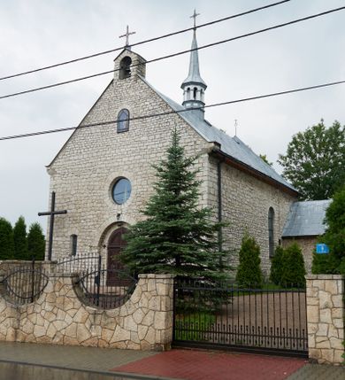 Zdjęcie nr 7: Kościół Najświętszej Marii Panny Królowej jest zlokalizowany w centrum Będkowic, na zachód od głównej drogi. Teren przykościelny jest otoczony wysokim murem posadowionym na kamiennej podmurówce oraz słupkach z nieregularnych ciosów kamienia i z żeliwnym płotem. W części wschodniej muru zlokalizowana jest szeroka brama, do której prowadzą schody, druga brama usytuowana jest nieco z prawej strony, również od wschodu.

Kościół jest skierowany na zachód, murowany, jednonawowy na rzucie prostokąta z prezbiterium zamkniętym półkoliście. Wnętrze tworzy szeroka nawa nakryta stropem oraz węższe i krótkie prezbiterium. Od północy przylega niewielka zakrystia na planie prostokąta z oknem od południa. Wejście do zakrystii zaznaczone jest drewnianym portalem. Na wschodniej ścianie nawy chór muzyczny, wsparty na dwóch słupach, dostępny klatką schodową od nawy. 

Nawę oświetlają dwa duże, rozglifione, prostokątne i zamknięte półkoliście okna umieszczone w południowej oraz północnej ścianie, a także dwa mniejsze okna ulokowane pod chórem zamknięte łukami odcinkowymi. Po bokach prezbiterium są dwa okrągłe okna. Wszystkie otwory okienne w nawie i prezbiterium wypełnione są witrażami lub ozdobnymi przeszkleniami. Do kościoła prowadzi główne wejście od strony wschodniej oraz jedno mniejsze od zakrystii.

Wygląd zewnętrznej elewacji kościoła jest skromny. Prezbiterium niższe od nawy, nad środkiem nawy wznosi się wieżyczka na sygnaturkę z latarnią, nakryta iglicą. Fasada prosta, w dolnej części wejście główne do świątyni, prostokątne, zamknięte łukiem półkolistym, powyżej okrągłe okno, a po bokach dwa mniejsze, prostokątne, zamknięte łukiem odcinkowym. W zwieńczeniu prostokątna, przeszklona, zamknięte półkoliście wnęka z figurą Chrystusa Frasobliwego, a na szczycie prosta aedikula z prześwitem, w której zawieszony jest mały dzwon. U góry łaciński krzyż na cokole. Otwory okienne i drzwiowe zdobione są kamienną okładziną. Świątynia nakryta jest dachem dwuspadowym.

