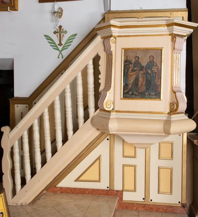 Zdjęcie nr 2: Ambona wisząca, przyścienna, z wejściem od lewej strony w postaci jednobiegowych schodów z balustradą. Kosz na planie czworoboku, na wypukłym cokole, flankowany na narożach spływami wolutowymi, od dołu ujęty niską szyszką; parapet w formie profilowanego gzymsu, wyłamanego nad osiami. Ścianki kosza zdobione prostokątnymi płycinami z malowanymi przedstawieniami czterech ewangelistów, ujętymi złoconymi ramami. Obraz umieszczony na ściance przedniej ambony przedstawia św. Mateusza oraz św. Łukasza w towarzystwie odpowiadających im atrybutów: człowieka i woła, a na obrazie na ściance bocznej ambony ukazano: św. Jana z orłem oraz św. Marka z lwem. Ewangeliści zostali przedstawieni frontalnie, w postawie stojącej, w delikatnym kontrapoście z prawą nogą ugiętą w kolanie. W prawych dłoniach trzymają pióra do pisania, a w lewych otwartą księgę (za wyjątkiem św. Marka, który w lewej dłoni trzyma pióro, a w prawej zamkniętą księgę). Święci ubrani są w długie suknie z długimi rękawami w kolorze niebieskim (św. Marek w kolorze różowym) oraz  żółte płaszcze (św. Jan — płaszcz w kolorze czerwonym, a św. Marek — w kolorze niebieskim). Święci mają charakterystyczne duże i bose stopy; twarze podłużne, z dużymi oczami i krótkimi brodami (św. Jan bez zarostu); włosy długie, zaczesane do tyłu. Wokół głów mają złote, koliste nimby. Tło obrazów stonowane, ugrowe. Święty Łukasz, św. Marek oraz człowiek i orzeł trzymają kałamarze. U dołu podpisy: „S(więty) Mateusz”, „S(więty) Łukasz”, „S(więty) Jon”, „S(więty) Marek". Struktura ambony polichromowana na beżowy kolor, a profilowania i detale złocone.
