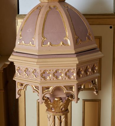 Zdjęcie nr 1: Stopa chrzcielnicy w formie ośmiobocznego, profilowanego cokołu, ustawionego na czworobocznej kostce. Stopa przechodząca u góry w ośmioboczną o opływowych kształtach. Trzon złożony z ośmiu kolumienek, zdobionych skręconym żłobkowaniem. Kapitel trzonu ośmioboczny, na każdej ściance ozdobiony liściem stylizowanego akantu. Czara ośmioboczna z ażurowymi arkadkami u spodu, każda ze ścianek czary zdobiona trzema małymi płycinami w formie czwórliści. Pokrywa na planie ośmioboku, zwężająca się ku górze, ze ściankami dekorowanymi zwężającymi się ku górze płycinami, zwieńczona niskim cokołem z rzeźbioną sceną Chrztu Chrystusa. Po lewej stronie Chrystus w delikatnym kontrapoście. Jest ubrany w czerwony płaszcz z niebieskim podbiciem. Ma podłużną twarz o małych oczach, wąskim nosie i ustach; ciemnobrązowe wąsy i brodę, która dzieli się w dwa pukle i falowane włosy opadające na kark. Z jego lewej strony na skale stoi św. Jan Chrzciciel, który prawą rękę z muszlą w dłoni unosi ponad głową Chrystusa i polewa go wodą. Ma owalną twarz o podobnym do Chrystusa wyrazie i wywijające się średniej długości włosami opadającymi na plecy. Jest ubrany w szatę ze skóry wielbłąda, odsłaniającą prawe ramię, a na nią ma zarzucony fioletowy płaszcz z szarym podbiciem. Struktura chrzcielnicy polichromowana w kolorze beżowym, stopa oraz płyciny w kolorze jasnego fioletu, zdobienia złocone, polichromia postaci naturalistyczna. 