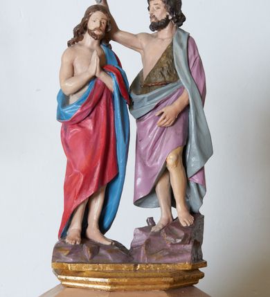 Zdjęcie nr 2: Stopa chrzcielnicy w formie ośmiobocznego, profilowanego cokołu, ustawionego na czworobocznej kostce. Stopa przechodząca u góry w ośmioboczną o opływowych kształtach. Trzon złożony z ośmiu kolumienek, zdobionych skręconym żłobkowaniem. Kapitel trzonu ośmioboczny, na każdej ściance ozdobiony liściem stylizowanego akantu. Czara ośmioboczna z ażurowymi arkadkami u spodu, każda ze ścianek czary zdobiona trzema małymi płycinami w formie czwórliści. Pokrywa na planie ośmioboku, zwężająca się ku górze, ze ściankami dekorowanymi zwężającymi się ku górze płycinami, zwieńczona niskim cokołem z rzeźbioną sceną Chrztu Chrystusa. Po lewej stronie Chrystus w delikatnym kontrapoście. Jest ubrany w czerwony płaszcz z niebieskim podbiciem. Ma podłużną twarz o małych oczach, wąskim nosie i ustach; ciemnobrązowe wąsy i brodę, która dzieli się w dwa pukle i falowane włosy opadające na kark. Z jego lewej strony na skale stoi św. Jan Chrzciciel, który prawą rękę z muszlą w dłoni unosi ponad głową Chrystusa i polewa go wodą. Ma owalną twarz o podobnym do Chrystusa wyrazie i wywijające się średniej długości włosami opadającymi na plecy. Jest ubrany w szatę ze skóry wielbłąda, odsłaniającą prawe ramię, a na nią ma zarzucony fioletowy płaszcz z szarym podbiciem. Struktura chrzcielnicy polichromowana w kolorze beżowym, stopa oraz płyciny w kolorze jasnego fioletu, zdobienia złocone, polichromia postaci naturalistyczna. 