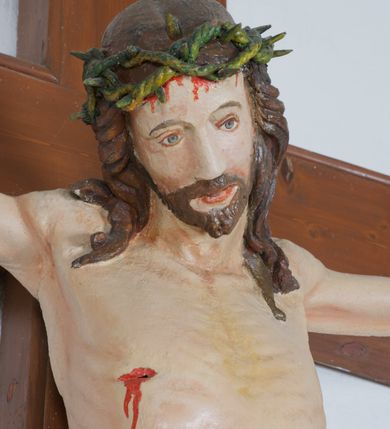 Zdjęcie nr 2: Do krzyża przybita trzema gwoździami figura Chrystusa na szeroko rozpiętych ramionach, z nogami ugiętymi w kolanach, założonymi prawa na lewą. Chrystus został przedstawiony w typie Cristo vivo, ze spuszczoną na prawe ramię głową, z otwartymi oczami. Spod zielonej korony cierniowej spływają na ramiona i plecy ciemnobrązowe, długie włosy. Biodra ciasno okryte czerwonym perizonium przewiązanym na prawym boku, z końcem układającym się w drobne, kaskadowe fałdy. Sylwetka szczupła o podkreślonej linii żeber; na ciele widoczne ślady Męki. Nad głową Chrystusa titulus w formie banderoli z napisem: „INRI”. Krzyż gładki, brązowy; polichromia w odsłoniętych partiach ciała naturalistyczna.  