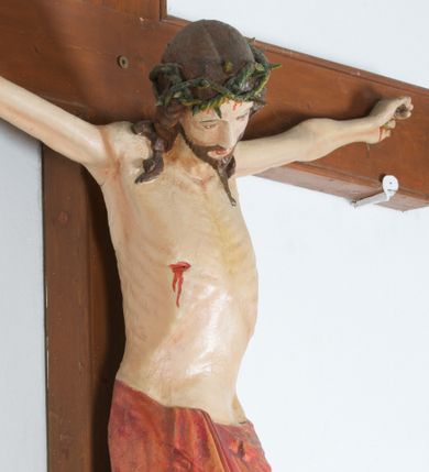 Zdjęcie nr 1: Do krzyża przybita trzema gwoździami figura Chrystusa na szeroko rozpiętych ramionach, z nogami ugiętymi w kolanach, założonymi prawa na lewą. Chrystus został przedstawiony w typie Cristo vivo, ze spuszczoną na prawe ramię głową, z otwartymi oczami. Spod zielonej korony cierniowej spływają na ramiona i plecy ciemnobrązowe, długie włosy. Biodra ciasno okryte czerwonym perizonium przewiązanym na prawym boku, z końcem układającym się w drobne, kaskadowe fałdy. Sylwetka szczupła o podkreślonej linii żeber; na ciele widoczne ślady Męki. Nad głową Chrystusa titulus w formie banderoli z napisem: „INRI”. Krzyż gładki, brązowy; polichromia w odsłoniętych partiach ciała naturalistyczna.  
