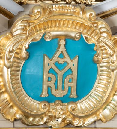 Zdjęcie nr 6: Rzeźby aniołków ukazane są w pozycji siedzącej, zwrócone ku sobie w lustrzanym odbiciu, z głowami uniesionym do góry i z rękami na wysokości piersi, z szeroko rozpostartymi skrzydłami; w pasie przewiązane są złotą chustą. Mają subtelny modelunek ciała. Twarze ich są okrągłe, z pucułowatymi policzkami. Włosy średniej długości, ciemnobrązowe, zasłaniające uszy. Polichromia w odsłoniętych partiach ciała naturalistyczna, skrzydła i chusta złocone. 
