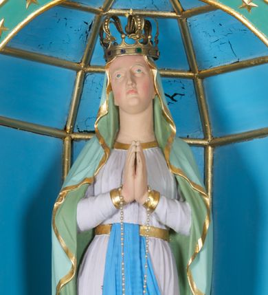 Zdjęcie nr 1: Rzeźba z przedstawieniem Matki Boskiej z Lourdes, ukazana frontalnie w postawie stojącej, z rękami złożonymi w geście modlitwy, z głową delikatnie uniesioną do góry. Matka Boska ubrana w jasnoróżową suknię, obwiedzioną na brzegach złotymi lamówkami, przewiązaną w talii złotym pasem z błękitną szarfą i jasnozielony płaszcz założony na głowę i spływający delikatnymi falami wzdłuż całej postaci, na brzegach obwiedziony złotą lamówką. Twarz owalna z długim i wąskim nosem, z wyraźnie zaznaczonym podbródkiem, ze wzrokiem skierowanym do góry, z zarumienionymi policzkami; na głowie korona w typie zamkniętym. Polichromia w odsłoniętych partiach ciała naturalistyczna.

