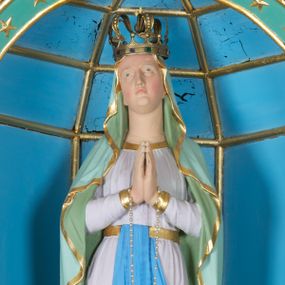 Zdjęcie nr 1: Rzeźba z przedstawieniem Matki Boskiej z Lourdes, ukazana frontalnie w postawie stojącej, z rękami złożonymi w geście modlitwy, z głową delikatnie uniesioną do góry. Matka Boska ubrana w jasnoróżową suknię, obwiedzioną na brzegach złotymi lamówkami, przewiązaną w talii złotym pasem z błękitną szarfą i jasnozielony płaszcz założony na głowę i spływający delikatnymi falami wzdłuż całej postaci, na brzegach obwiedziony złotą lamówką. Twarz owalna z długim i wąskim nosem, z wyraźnie zaznaczonym podbródkiem, ze wzrokiem skierowanym do góry, z zarumienionymi policzkami; na głowie korona w typie zamkniętym. Polichromia w odsłoniętych partiach ciała naturalistyczna.
