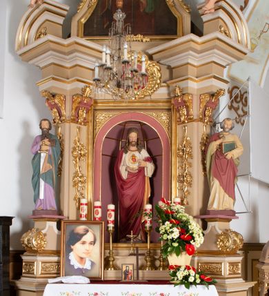 Zdjęcie nr 1: Ołtarz architektoniczny, jednokondygnacyjny, jednoosiowy, ze zwieńczeniem. Ołtarz drewniany, prostopadłościenny, z drewnianą mensą i kamiennym portatylem. Mensa ustawiona na niskim stopniu, na ściance frontowej zdobiona płyciną w kształcie leżącego prostokąta z płaskorzeźbionym monogramem IHS w polu. Nastawa ołtarzowa na zdwojonym cokole, ujęta parą ukośnie ustawionych filarów, podtrzymujących przerwane nad osią środkową belkowanie z silnie wysuniętym gzymsem i ukośnie ustawionym przerwanym, segmentowym przyczółkiem z usadzoną na nim parą aniołków. W polu środkowym głęboka, trójboczna wnęka, zamknięta półkoliście, z rzeźbą Najświętszego Serca Pana Jezusa, ujęta prostokątną, profilowaną ramą. Nad polem środkowym owalny kartusz z monogramem IHS na czerwonym polu, ujęty ornamentyką roślinną. Retabulum flankowane parą rzeźb: św. Piotra po prawej i św. Pawła po lewej stronie, ustawionych na wolutowych cokołach.

Zwieńczenie w kształcie stojącego prostokąta o uciętych bokach ujętych spływami wolutowymi, zamknięte gzymsem w formie łuku nadwieszonego, z ażurową, rocaille’ową dekoracją u szczytu; w polu obraz z przedstawieniem św. Barbary. Gzyms zdobiony rzędem stylizowanych palmetek. Trzony podpór zdobione dwiema, splecionymi gałązkami róży, spiętymi u góry karbowaną wstęgą; kapitele w formie konsolek w kształcie esownicy, zdobione ornamentyką stylizowanych akroterionów akantowych.

Struktura polichromowana w kolorze beżowym; wnęka i kapitele w kolorze różowym; ornamentyka i partie detalu architektonicznego złocone.    
